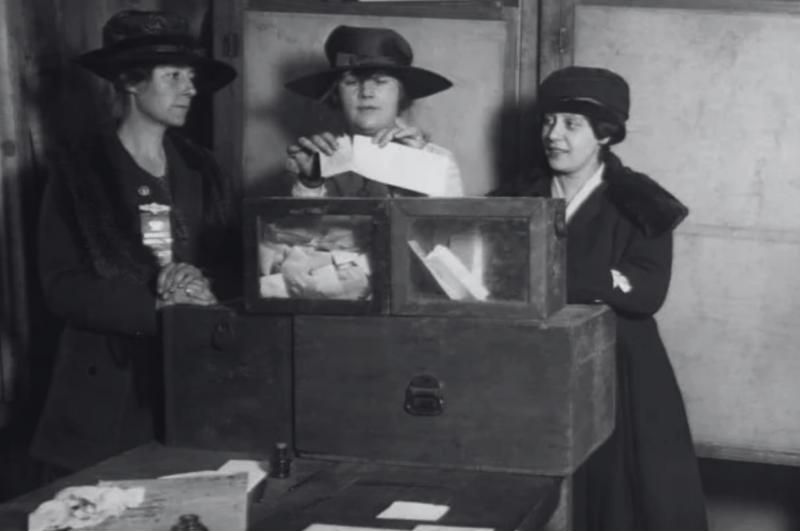 Três mulheres de chapéu depositando votos numa urna, em foto preto e branco