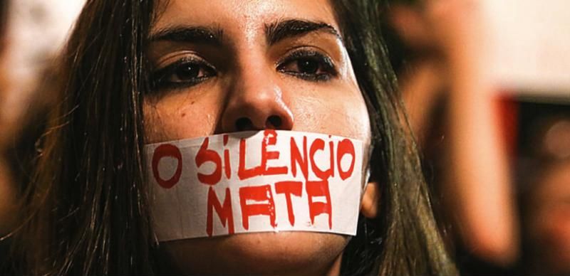 Mulher com fita na boca onde se lê O silêncio mata