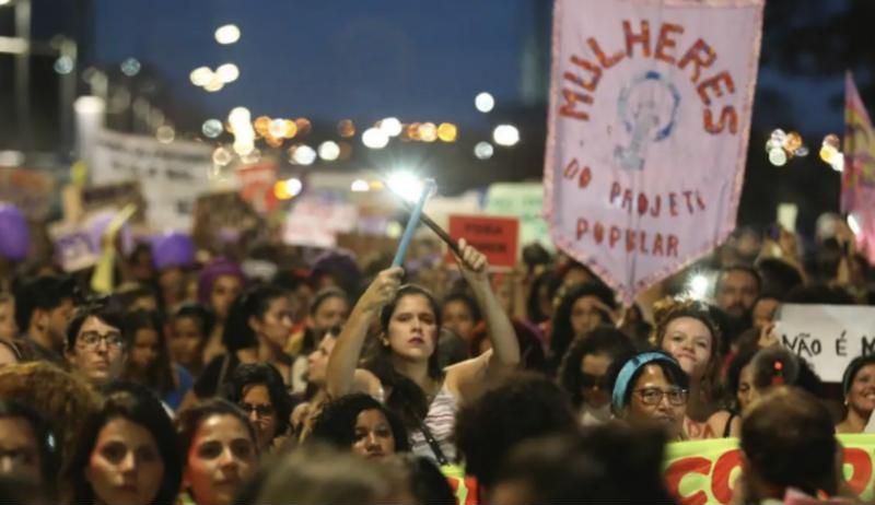 Multidão de mulheres em marcha noturna com faixas e bandeiras
