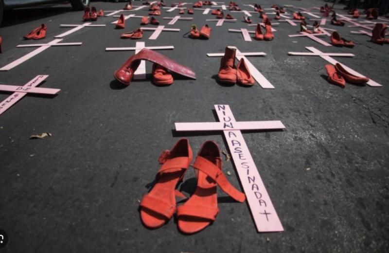 Sapatos vermelhos ao lado de cruzes rosas no asfalto, em protesto contra o feminicídio